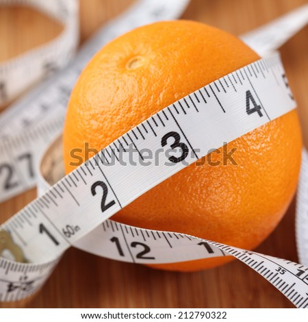 Orange wrapped in a tape measure. Diet concept. Shallow depth of field. Close-up.