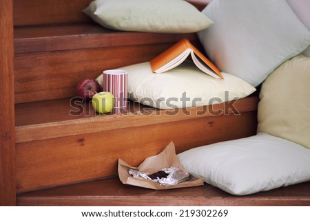 Stairs with book, apples, chocolate and a cup with a fresh drink and even pillows for comfortable reading.