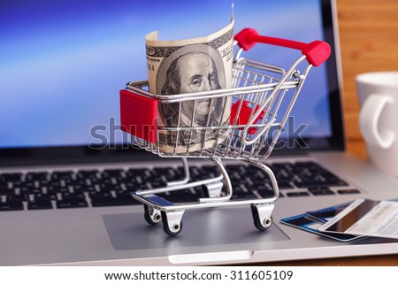 Online shopping. Shopping cart with one hundred dollars bill on laptop.