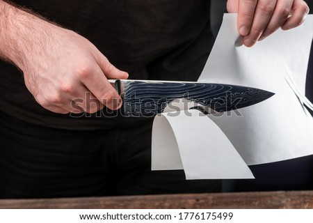 Man testing sharpness of knife by cutting a thin sheet of paper. Japanese Gyuto knife with Damascus steel blade.