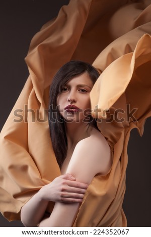 Brunette woman wrapped in gold cloth posing.  Background gold cloth and black.Hands close to the her body