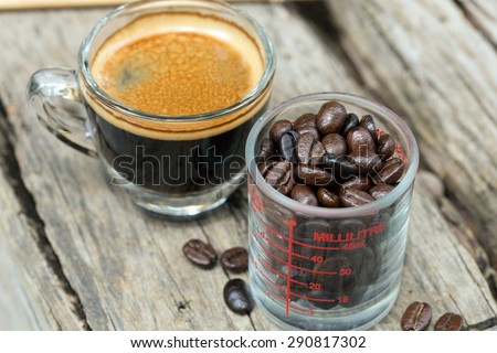 Coffee beans in a glass measuring cup and Espresso coffee cup on the table.