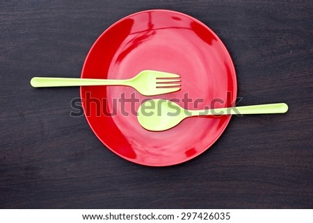 Red empty plate, spoon and fork green plastic on a wooden table.