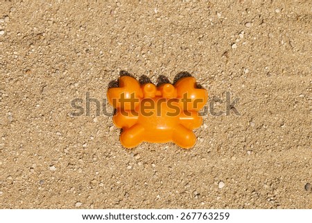 An orange toy crab shape on top of sand in a playground (horizontal shot).  The toy is centered in the middle of the image.