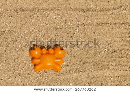 An orange toy crab shape on top of sand in a playground (horizontal shot).