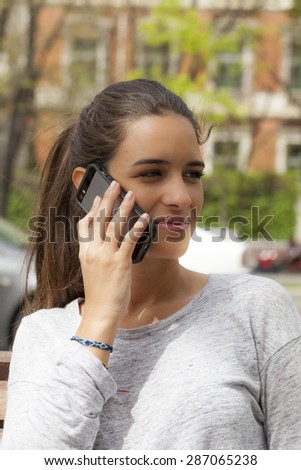 A young woman talking on a cell-phone looking to her left; outdoors in a city. Vertical Shot.