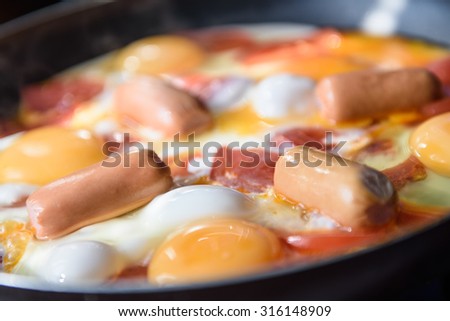 fried eggs with sausages and tomatoes on a hot pan, cooking breakfast