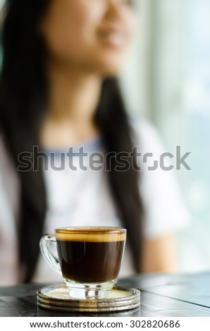 The cup of coffee (espresso) on the wooden table in the coffee shop with woman background