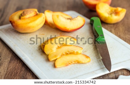 cut slices of ripe peach on a white board, green knife on wooden background