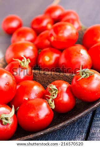 red juicy tomatoes cherry in brown wooden plate, vertically