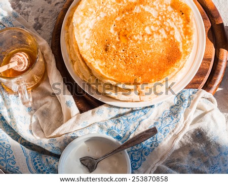 many subtle sweet pancakes with honey and sour cream on a wooden board, rustic, top view