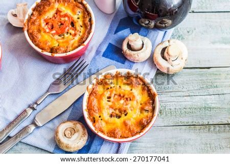 Baked mushroom julienne with tomato and cheese in red pots, top view, lunch on gray board