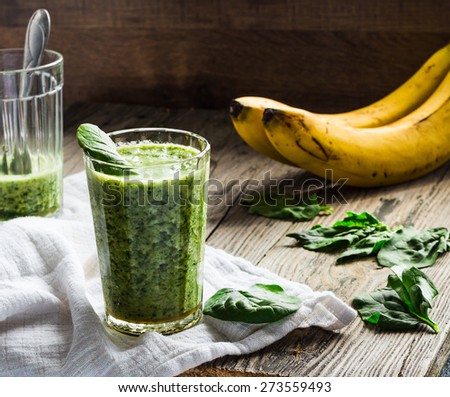 green smoothie with spinach leaves, banana with peanut milk in a glass on a gray wooden background