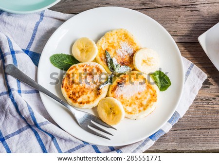 pancakes from cottage cheese  with banana, powdered sugar and fresh mint, gray wooden background, breakfast