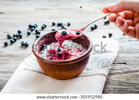 eating a banana ice cream with blueberries and coconut spoon, hand, healthy dessert, vegan, rustic background