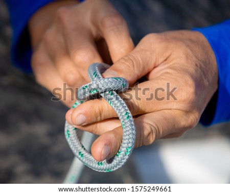Closeup male hands with knotted rope, ropee knot, sailing rope in hands, man's hands closeup learning how to tie a bowline knot