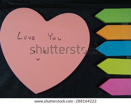 Love you with smiling face, drawing and writing on pose it paper with colorful heart and arrow on black skin background