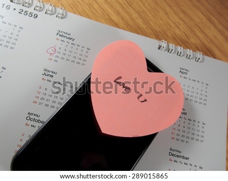 Love you writing on sticker paper with pink heart shape and mobile phone, calender with marking on February 14th