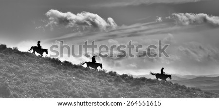 Ridge Riders in Black and White - silhouettes of Cowboys and Horses riding down a ridge.  Dramatic clouds above them and range below them.