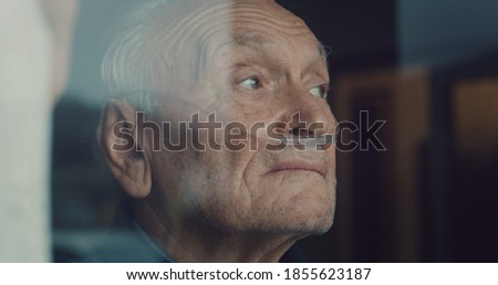 Cinematic close up shot of an elderly thoughtful man wearing oxygen tube is looking through a window in the morning. Concept of healthcare, life, pensioner, grandparents, retirement, boarding house.