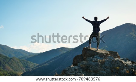 On the edge of a rocky cliff a man raises his hands to heaven as a sign of freedom or victory and in the background a fantastic landscape. Concept of: breathing, freedom, journey, life, love. Foto d'archivio © 