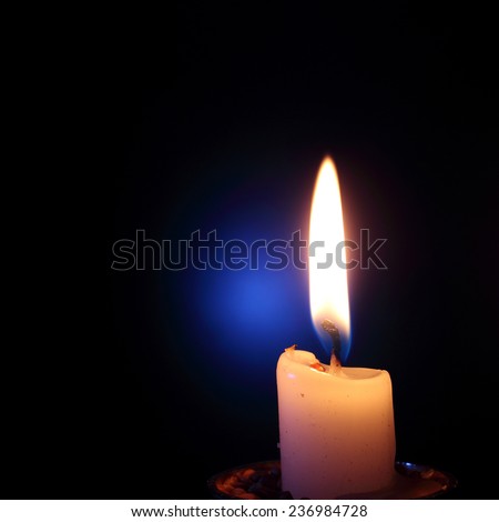 The burning candle on a black background with a blue patch of light