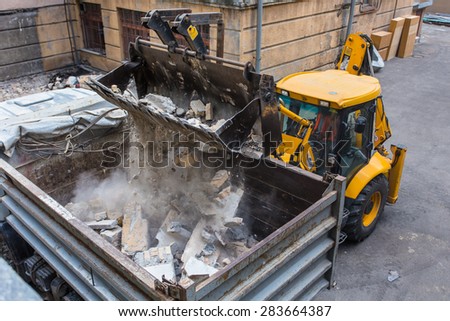 Loader loading truck with gravel and bricks in city yard
