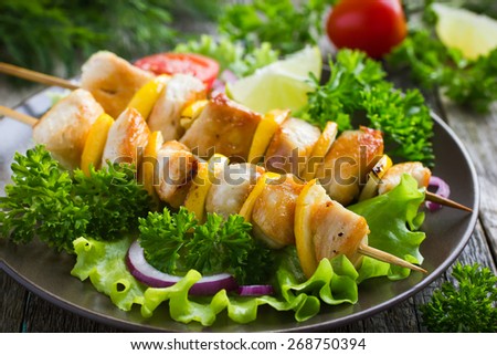 Grilled chicken and lemon kebabs on wooden background