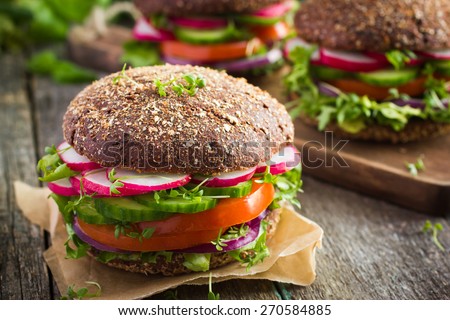 Healthy fast food. Vegan rye burger with fresh vegetables on old wooden  background