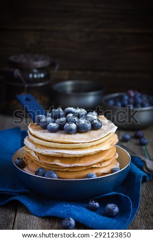 pancakes with blueberry and powdered sugar in pan on rustic background