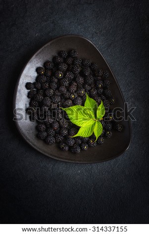 Fresh blackberry and green leaf on black plate. top view