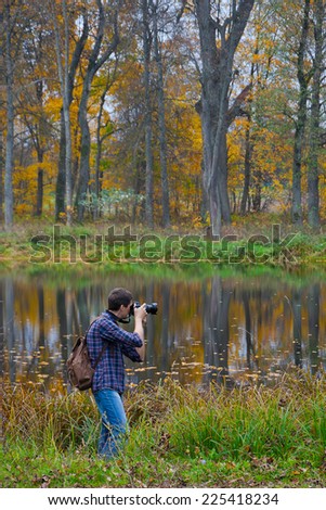 Photographer in a check shirt takes off an autumn park with a lake