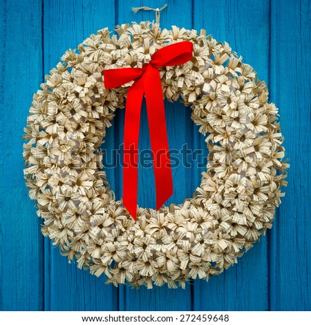 Paper wreath with red ribbon hanging on a blue wooden wall