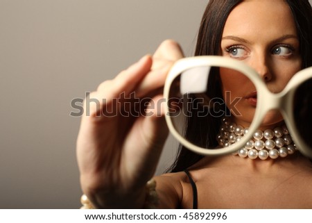 Fashion model holding big white sunglasses and pearls necklace.