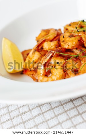 King prawns dish with a slice of lemon and garlic chives on white plate, cropped close up