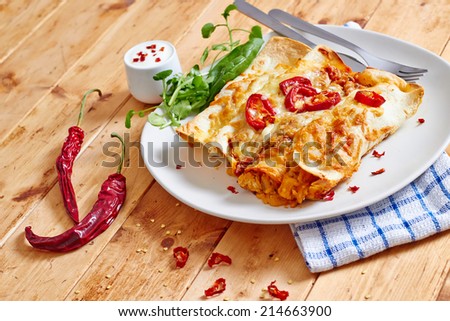 Enchiladas dish with chili peppers on a wooden table with salad, wide view