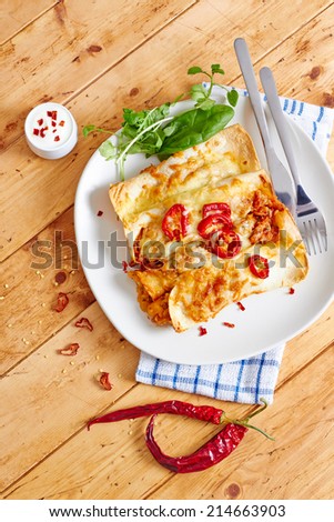 Enchiladas dish with chili peppers and melted cheese with creme on a wooden table, top view