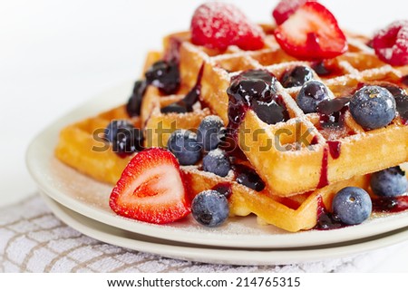 Waffles with honey, jam, and berries on a white plate, in close up view