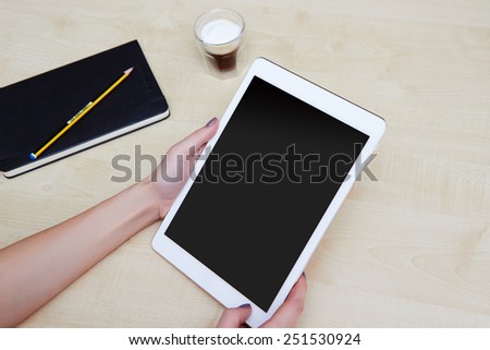 Hands holding digital tablet on a wooden desk with coffee and organiser