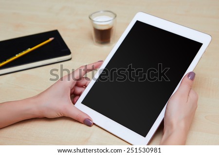 Hands holding digital tablet on a wooden desk with coffee and organiser, blank screen