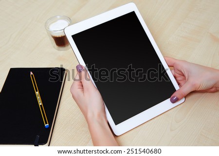 At the office girl working on a white digital tablet, on a wooden desk and a coffee