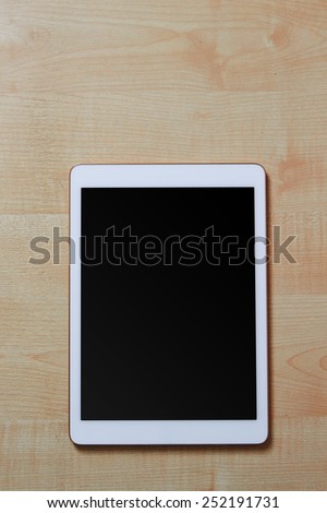 White digital tablet on a wooden desk with blank screen, space for text, top view