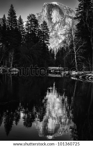 Black and white scenic view of snow capped mountain and forest reflected on lake.