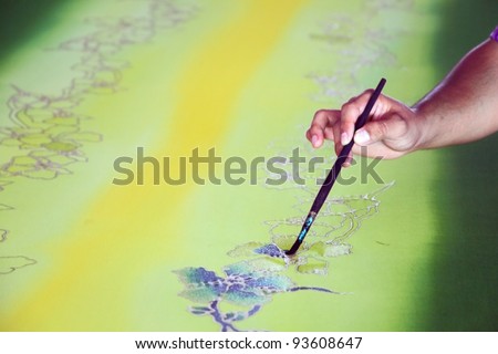 An artist carefully paint the floral/flower motif on a yellow traditional batik fabric