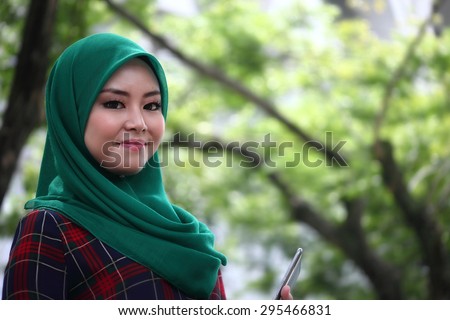 Asian muslimah wearing hijab in green park area with copy space area for advertising material