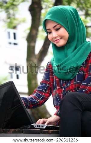 Young beautiful asian muslimah wearing hijab with laptop computer  in green outdoor park university campus  area