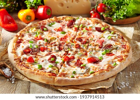 Pizza restaurant menu - Meat Pizza on parchment, topped off with meat hot sausage and pepperoni slice. Wooden table with pizza ingredients. Sunlight with harsh shadow. Rustic, natural style food