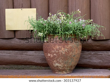 Bouquet of wild flowers in old vase on a background wooden texture. Rough piece of paper pinned to the wall with rusty key