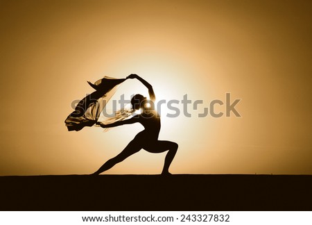 Silhouette of a young woman in a warrior yoga pose at sunset