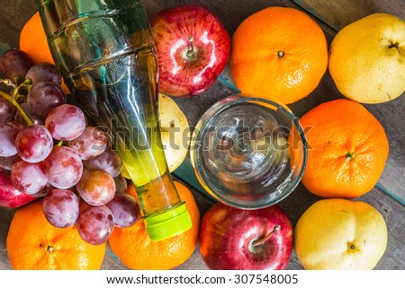 Bottle of juice and a glass placed on many of fruits.